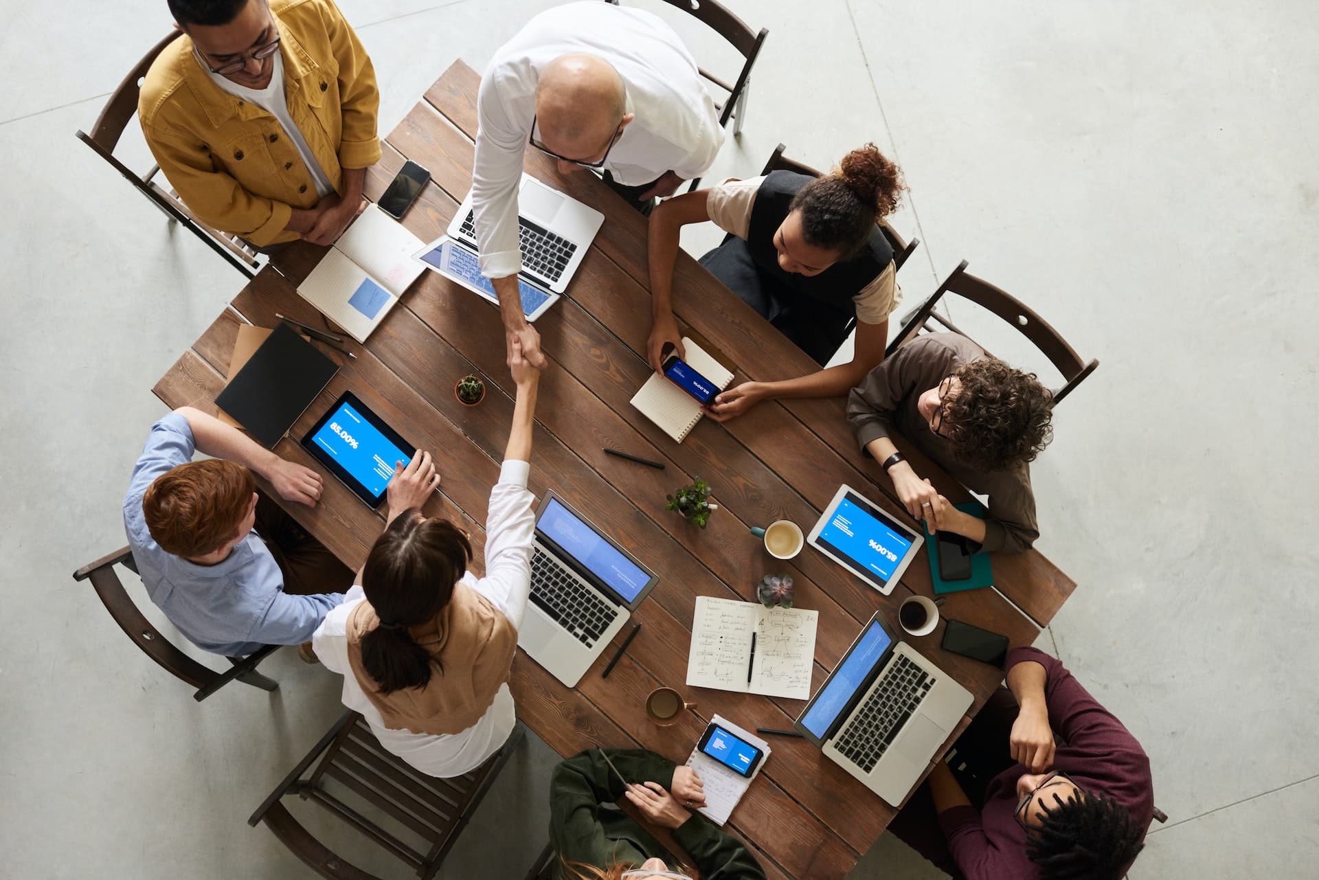 Foto do ambiente de trabalho de uma lawtech ou legaltech com mesa e seis pessoas sentadas, trabalhando e  utilizando notebooks, cadernos, Ipad e smartphones