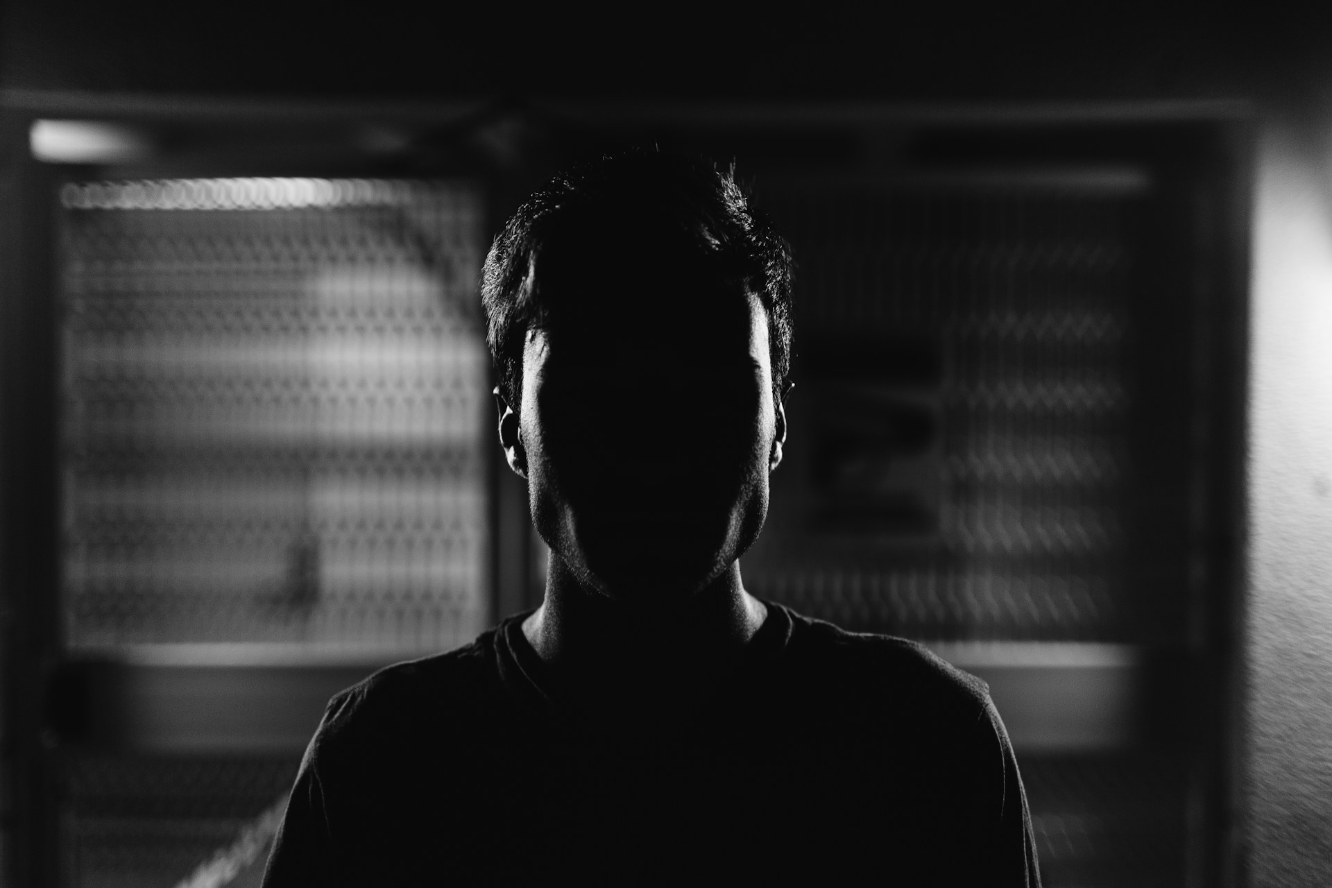 Foto em preto e branco da silhueta de um homem, cujo rosto está completamente nas sombras, simbolizando o anonimato e a proteção de identidade de um indivíduo em um acordo de colaboração premiada. 