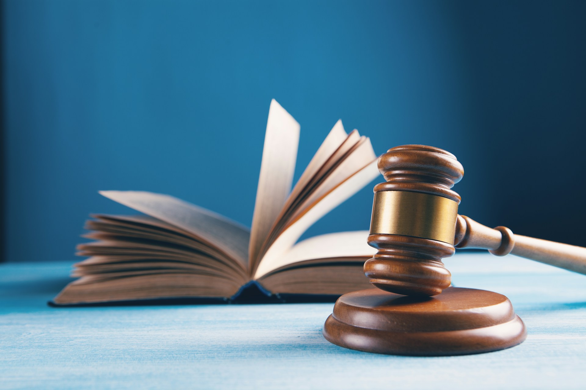 Foto de um martelo de juiz de madeira e sua base, com um livro de leis aberto ao fundo. A imagem simboliza a autoridade da justiça e as decisões baseadas na legislação, frequentemente associadas ao trabalho de tribunais superiores como o STF.
